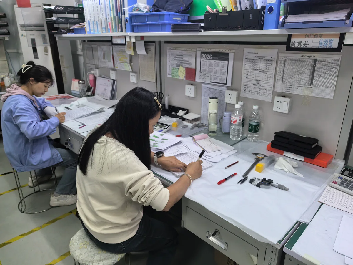 OUJI quality staff recording inspection results at a workbench with measurement tools and drawings