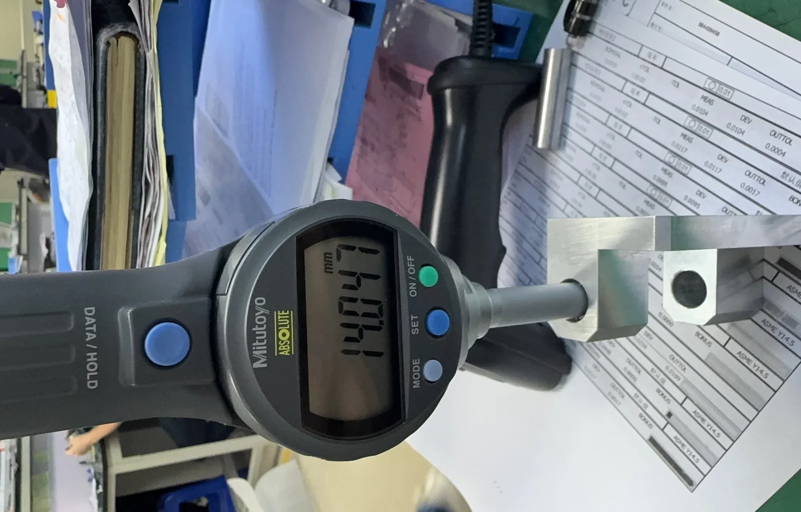 Mitutoyo digital height gauge measuring a machined block, with an inspection report referencing ASME Y14.5 visible beneath it
