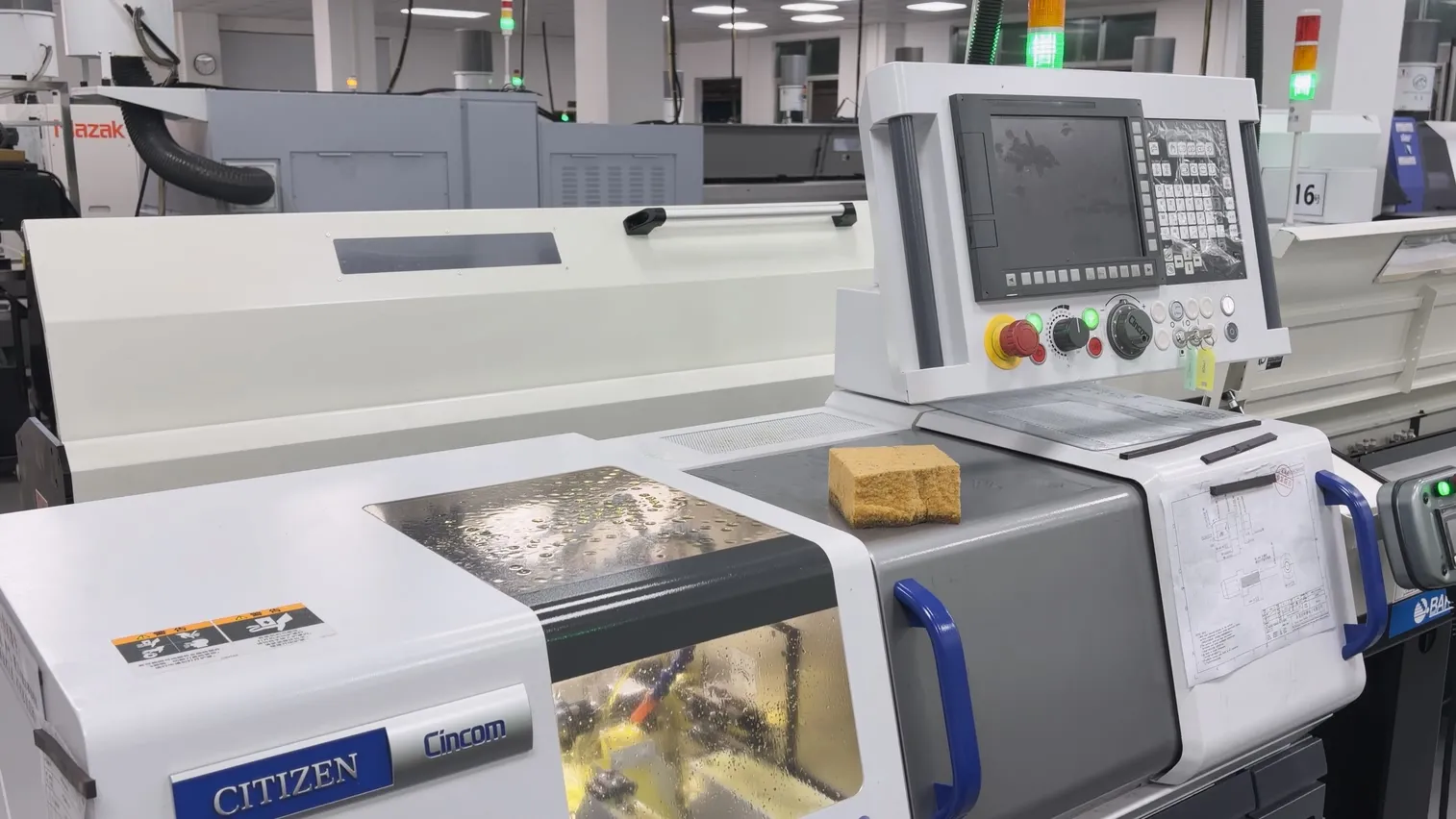 Citizen Cincom R04VI Swiss-type lathe with its bar feeder and a working drawing clipped beside the control panel