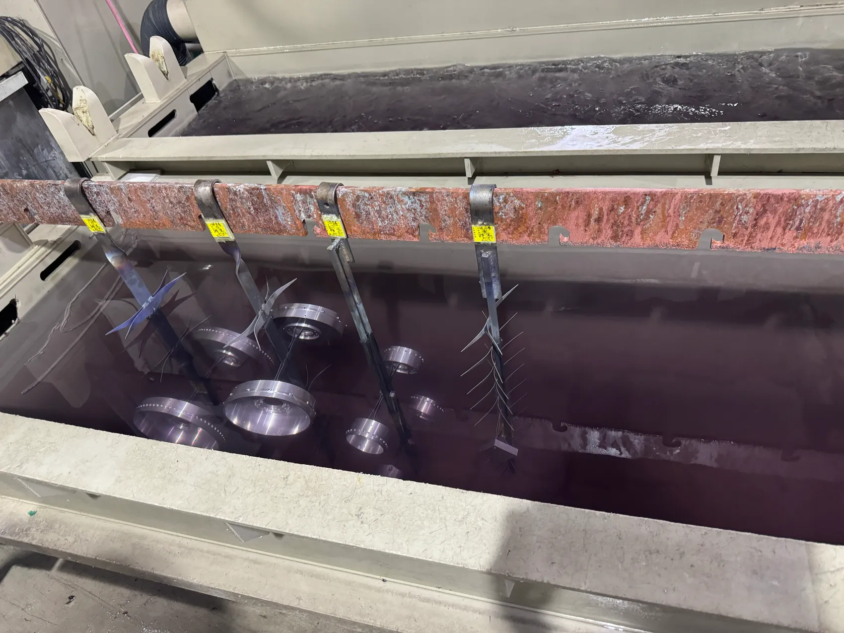 Machined aluminum housings on a rack, partially immersed in an anodizing tank