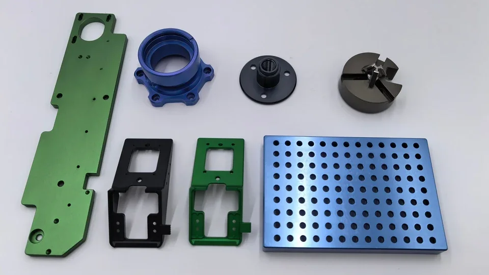 Seven real finished OUJI parts with green, blue and black surfaces, including frames, a flange and perforated plates