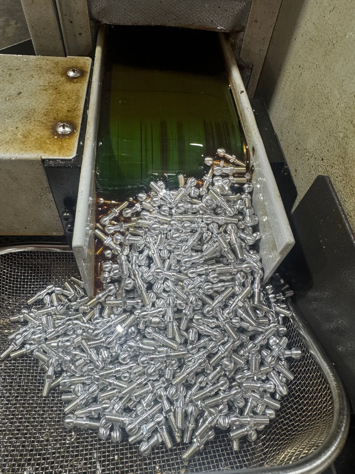A batch of small aluminum ball-head screws collected beside the machine outfeed