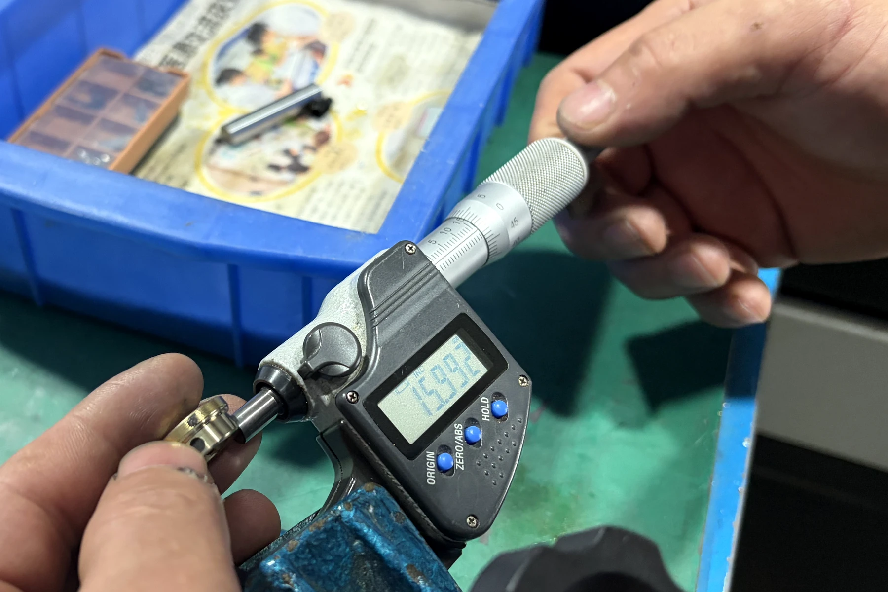 Digital micrometer displaying 15.992 mm while measuring the outside diameter of the finished brass bushing