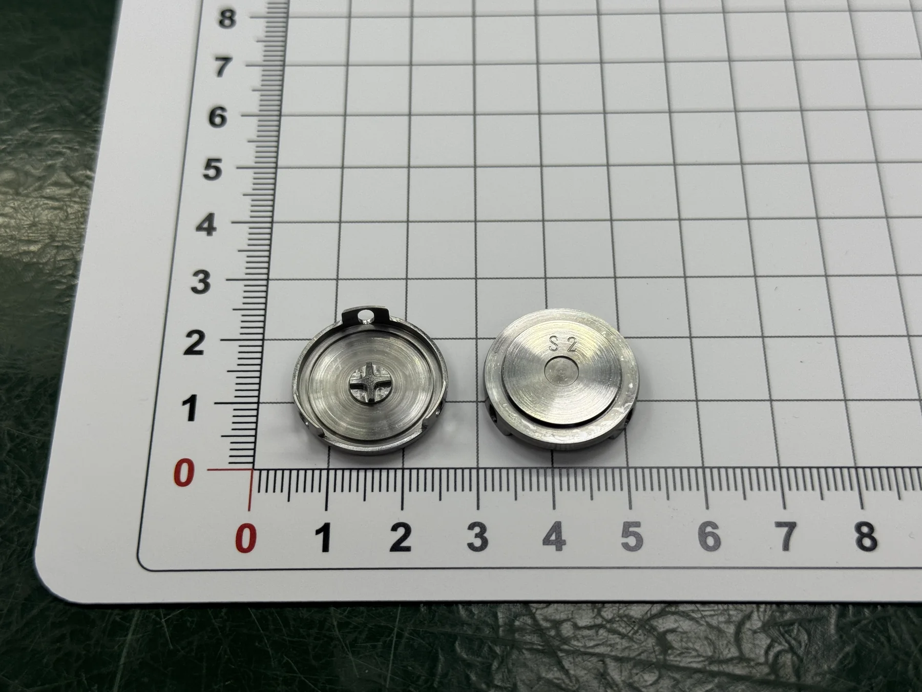 Two views of the finished SUS420J2 thin-wall part showing the internal cross feature and S2 marking