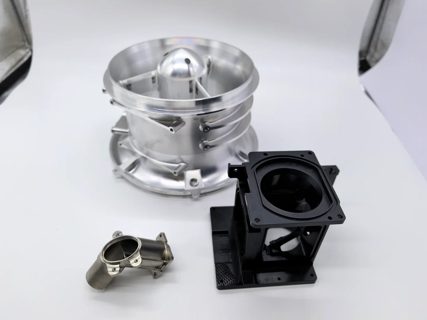 CNC machined components, including a cylindrical housing, a black rectangular housing and smaller flanged parts