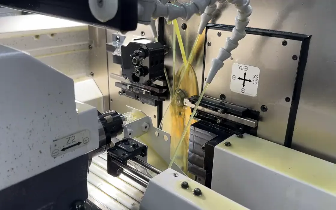 Swiss-type machining work area with tool slides, spindle and small workpiece under cutting oil