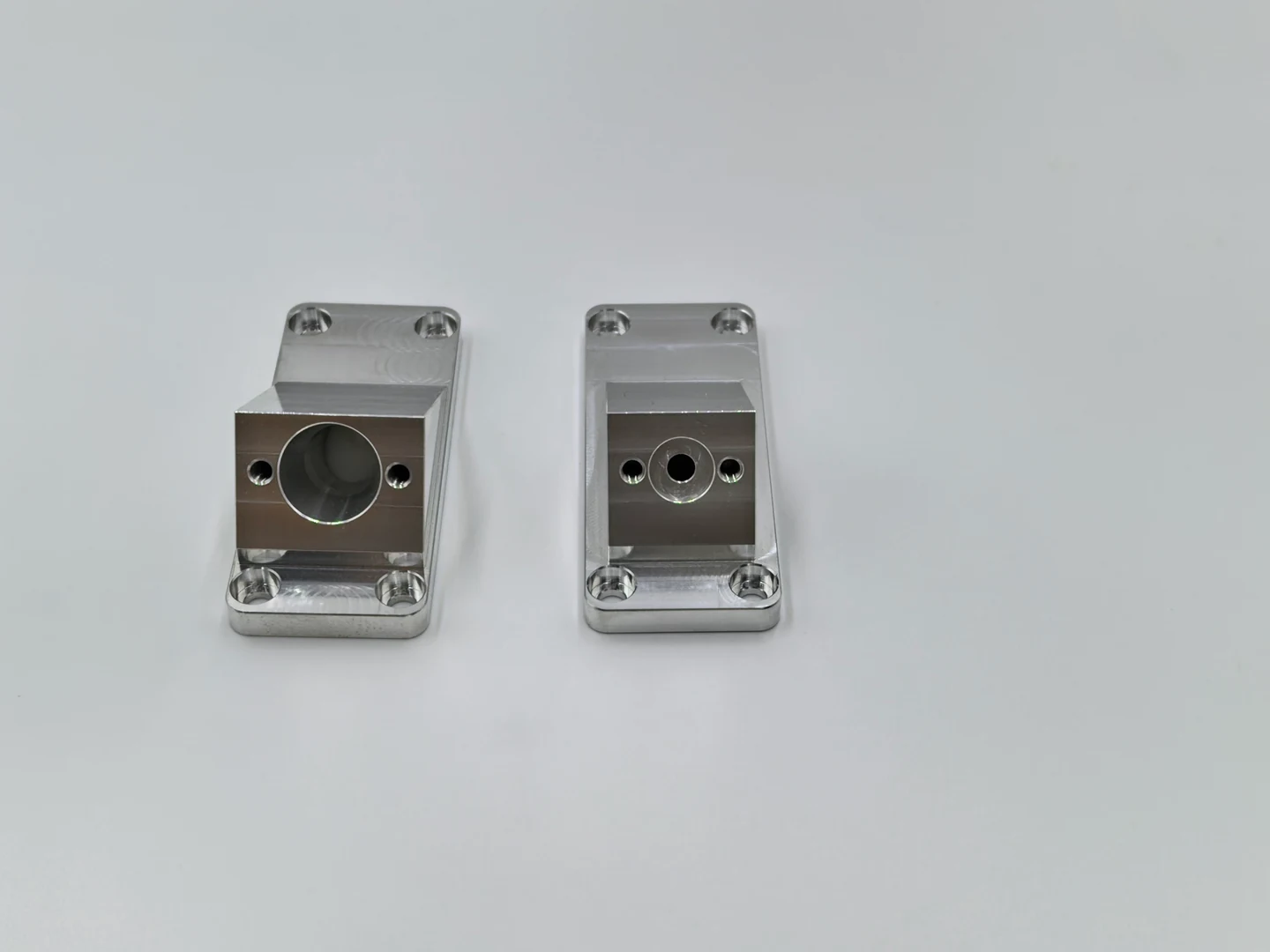 Two OUJI machined components with mounting holes and different central bores