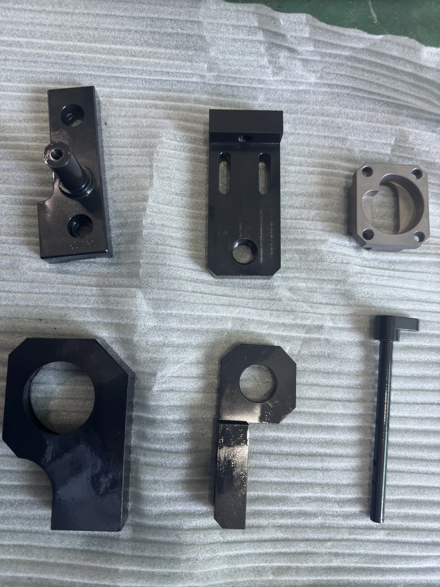 Six different OUJI machined components arranged on protective foam, with varied holes, slots and profiles