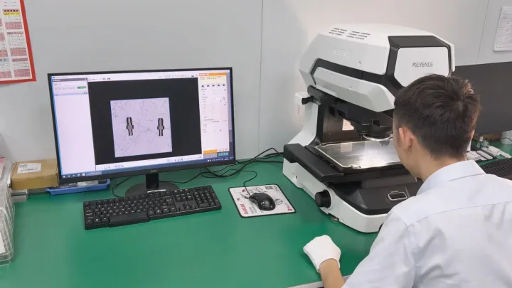 OUJI operator inspecting miniature turned components with a Keyence optical measuring system