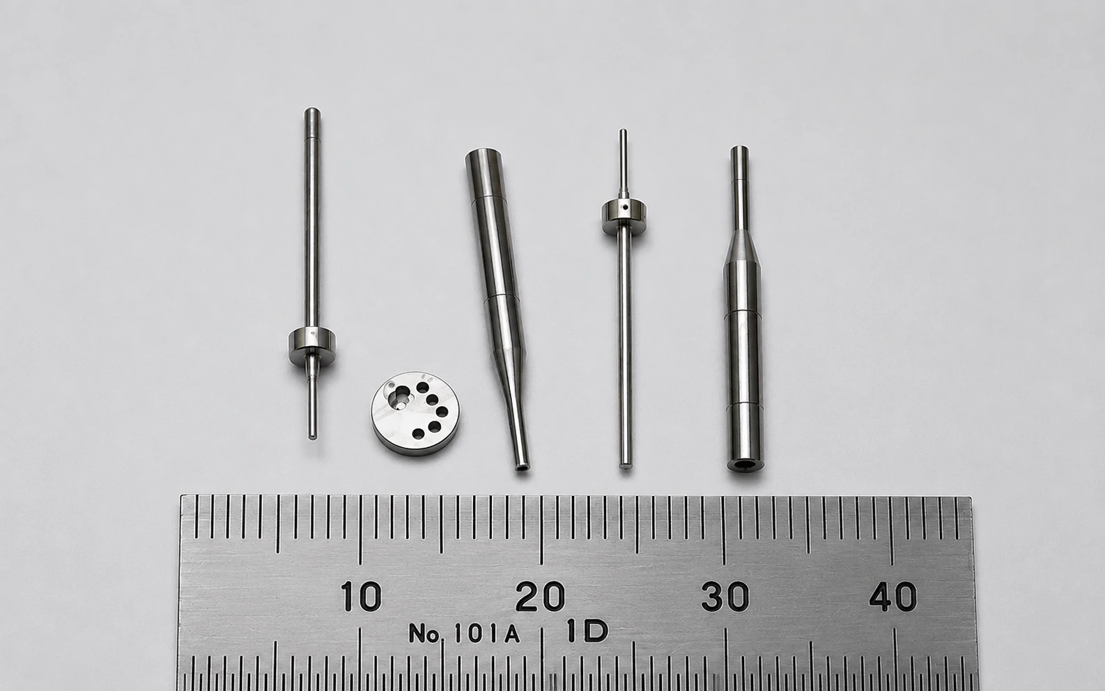 Micro-machined shafts, pins and precision turned parts under 4 mm beside a millimeter ruler